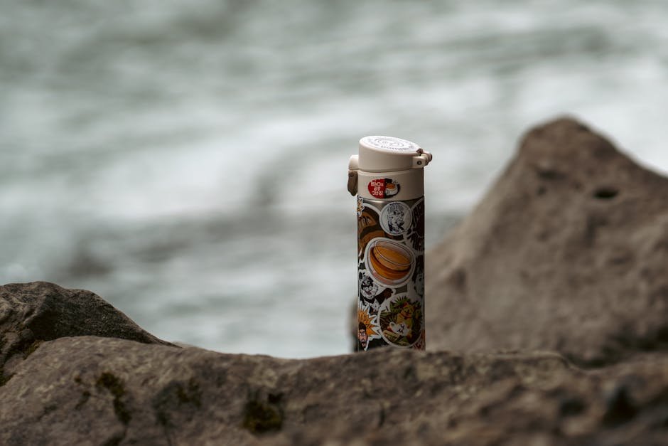 A vacuum flask decorated with stickers rests on rocks by a seashore in Russia.